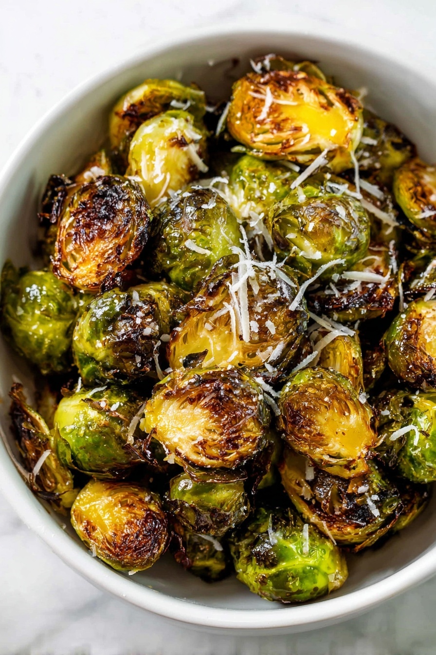 A white bowl filled with roasted Brussels sprouts halved and cooked until the edges are dark brown and crispy, showing a mix of bright green, golden yellow, and deep brown colors from caramelization, with a light sprinkle of shredded white cheese on top. The Brussels sprouts have a textured look with some charred parts and a slightly oily shine. The bowl sits on a white marbled surface. photo taken with an iphone --ar 2:3 --v 7