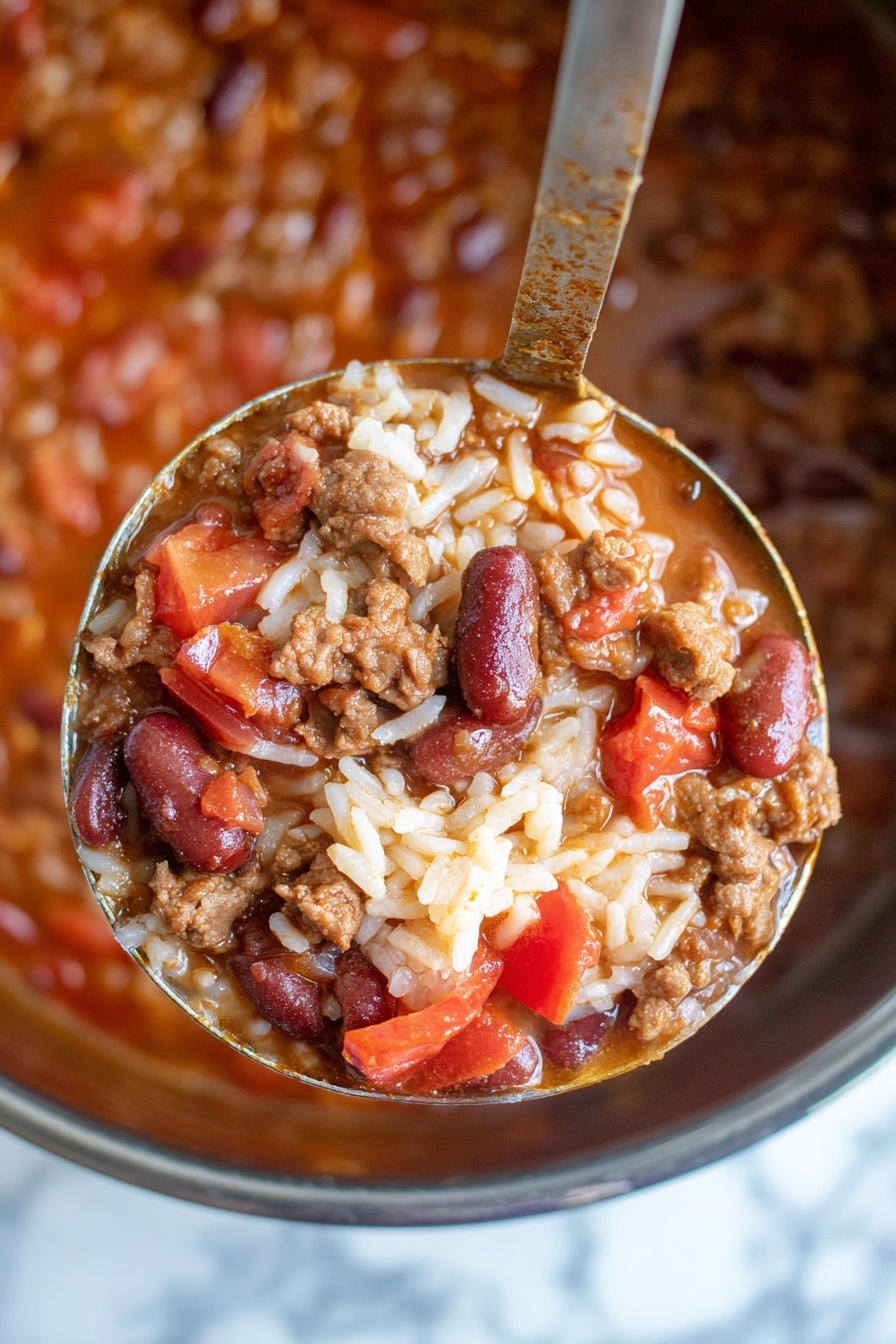 A close-up of a silver spoon holding a thick stew filled with white rice, brown ground meat, chunks of orange-red tomatoes, beans, and bits of onions. Below the spoon, a white bowl is full of the same stew, layered with yellow shredded cheese and a dollop of white sour cream on a white marbled surface with a colorful striped cloth in the background. Photo taken with an iphone --ar 2:3 --v 7