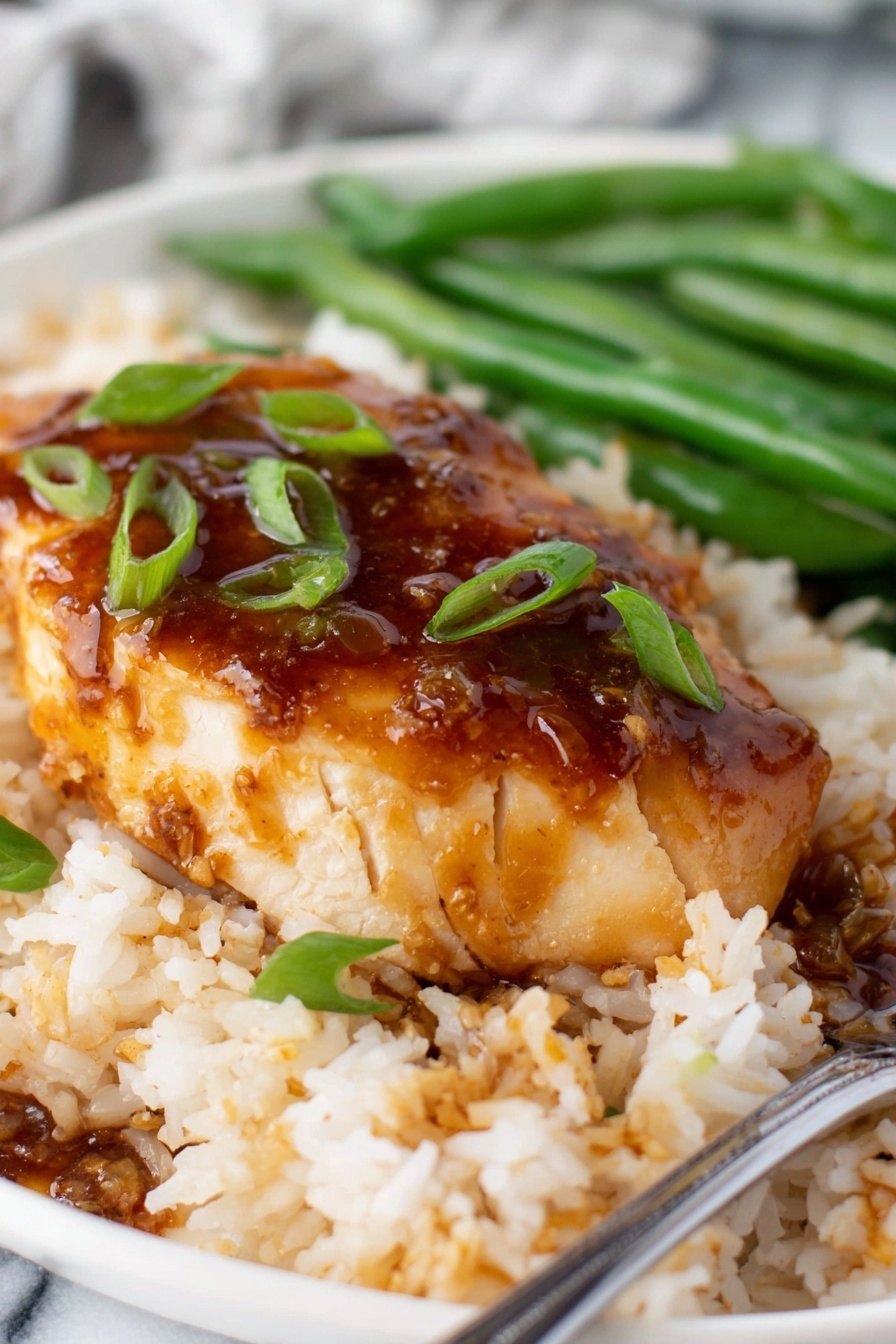 honey garlic chicken - Several pieces of cooked chicken fillets are in a pan, covered by a shiny brown sauce that looks thick and smooth. The chicken is golden brown and tender with small green onion pieces scattered on top. The sauce pools around the chicken, creating a glossy layer that highlights the texture of the meat underneath. The pan shows some browning marks from cooking. The background is a white marbled texture. Photo taken with an iphone --ar 2:3 --v 7