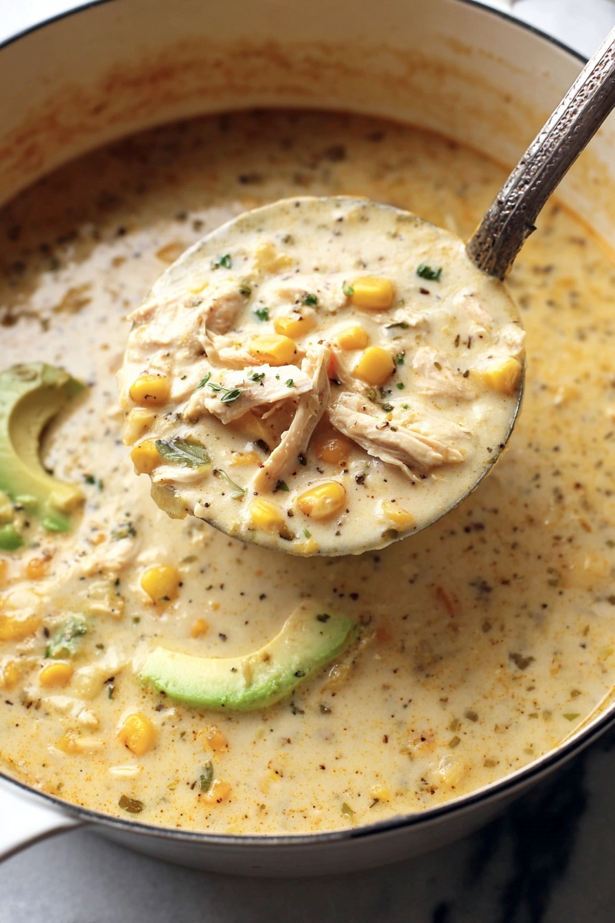 Creamy White Chicken Chili - A large ladle filled with thick creamy soup is being lifted from a white pot, showing three main layers: light creamy broth with specks of black pepper and chopped herbs, soft yellow corn kernels scattered throughout, and shredded white meat pieces visible near the surface. In the background, sliced green avocado adds a fresh color contrast. The soup’s texture looks rich and smooth with some visible small chunks. The pot sits on a white marbled surface. Photo taken with an iphone --ar 2:3 --v 7