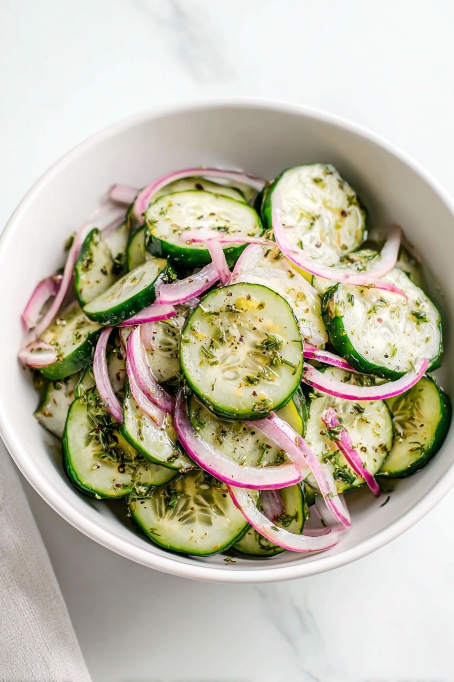 A white bowl filled with a cucumber salad sits on a white marbled surface. The salad has three main layers: thin green cucumber slices with dark green edges form the base, while thin slices of pink and white onion are mixed evenly throughout. The top layer is sprinkled with small pieces of dried green herbs adding a speckled look over the fresh vegetables. The cucumber slices show some natural seeds and light green flesh, and the onions have a slight shine, making the whole salad look fresh and crisp. photo taken with an iphone --ar 2:3 --v 7