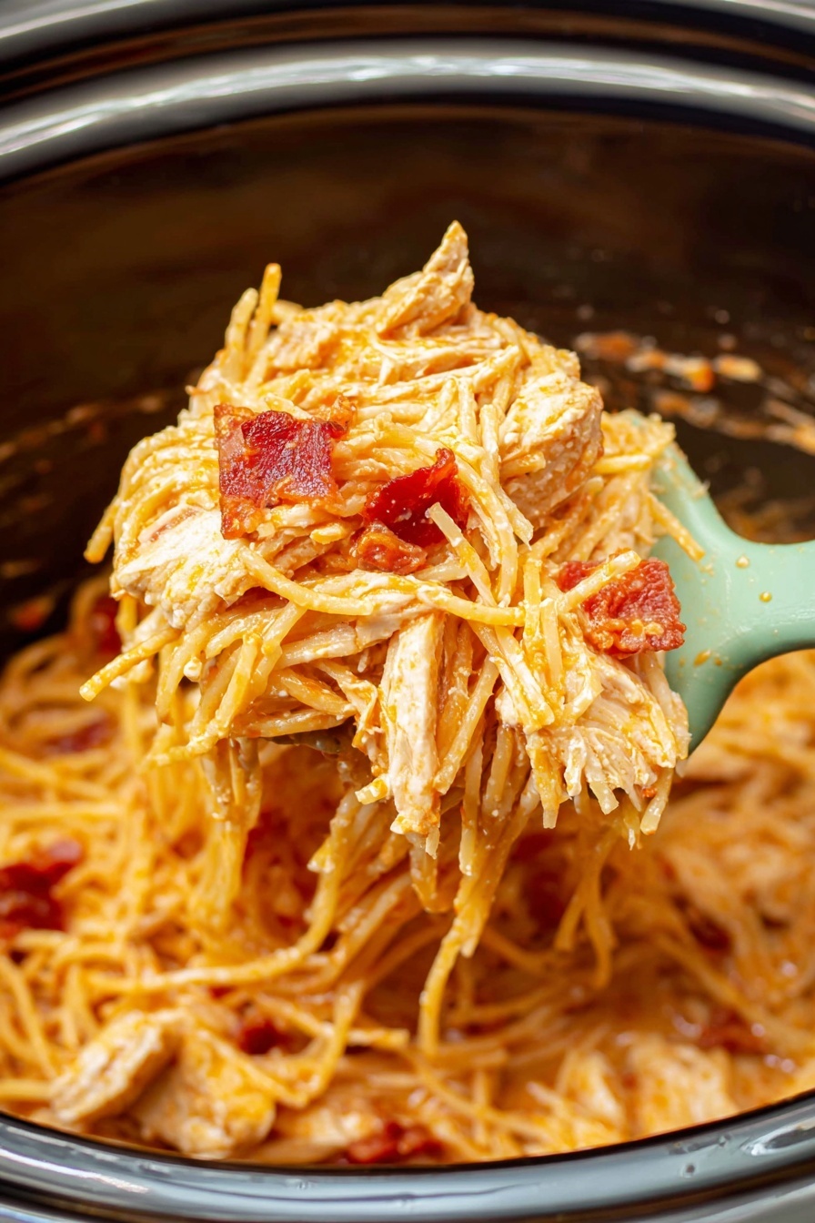 The image shows a close-up of creamy spaghetti mixed with chunks of cooked chicken and small pieces of red bacon, all coated in a light orange sauce. The pasta strands look soft and slightly glossy, entwined tightly together. The chicken pieces are white with a hint of brown from cooking, and the red bacon adds pops of color throughout. The food is held on a pale mint green spatula above a dark slow cooker, with the background inside the cooker showing some sauce splashes and texture. Photo taken with an iphone --ar 2:3 --v 7
