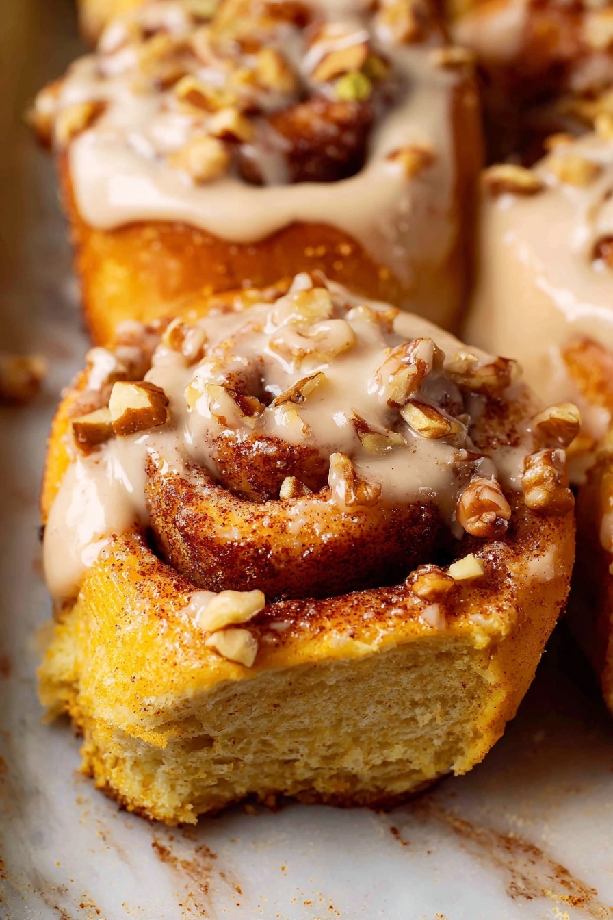The image shows a close-up of soft cinnamon rolls with three layers: the bottom layer is a golden-brown baked dough with a slightly crispy texture, the middle layer has swirls of cinnamon spice creating a rich, reddish-brown color, and the top layer is a creamy beige icing drizzled thickly over the rolls with pieces of chopped nuts sprinkled on the icing. The rolls are on a baking tray with a white marbled texture underneath them. The photo taken with an iphone --ar 2:3 --v 7