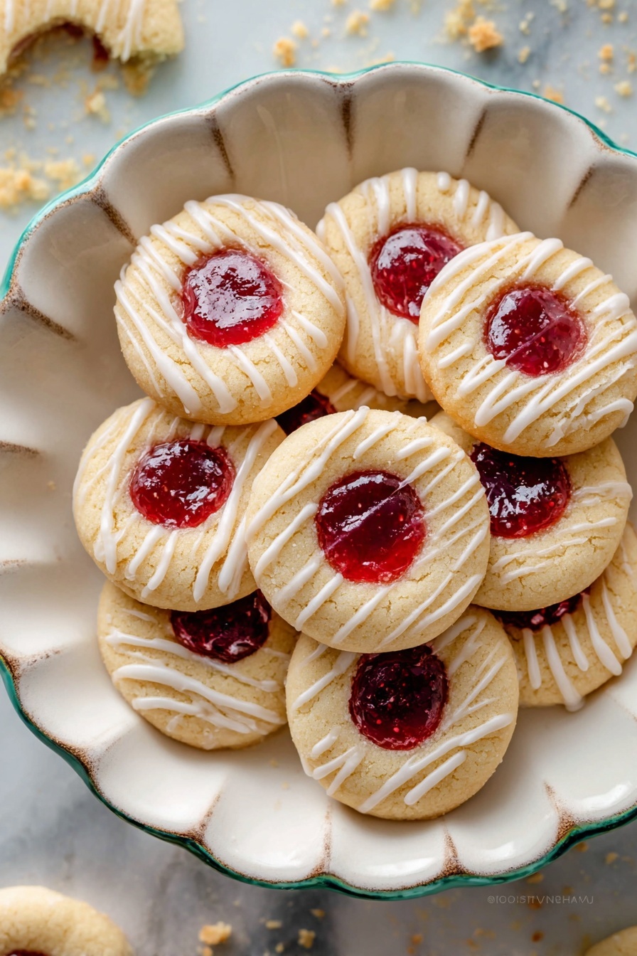 A white scalloped bowl filled with round thumbprint cookies, each cookie has a light golden base layer with a soft texture that looks slightly crumbly. In the center of each cookie is a bright red jam layer, smooth and shiny, sitting in a small well. The top layer features a thin drizzle of white icing in parallel lines across each cookie, adding a delicate decorative touch. The bowl is placed on a white marbled surface with cookie crumbs scattered around, showing a casual and inviting setting. photo taken with an iphone --ar 2:3 --v 7