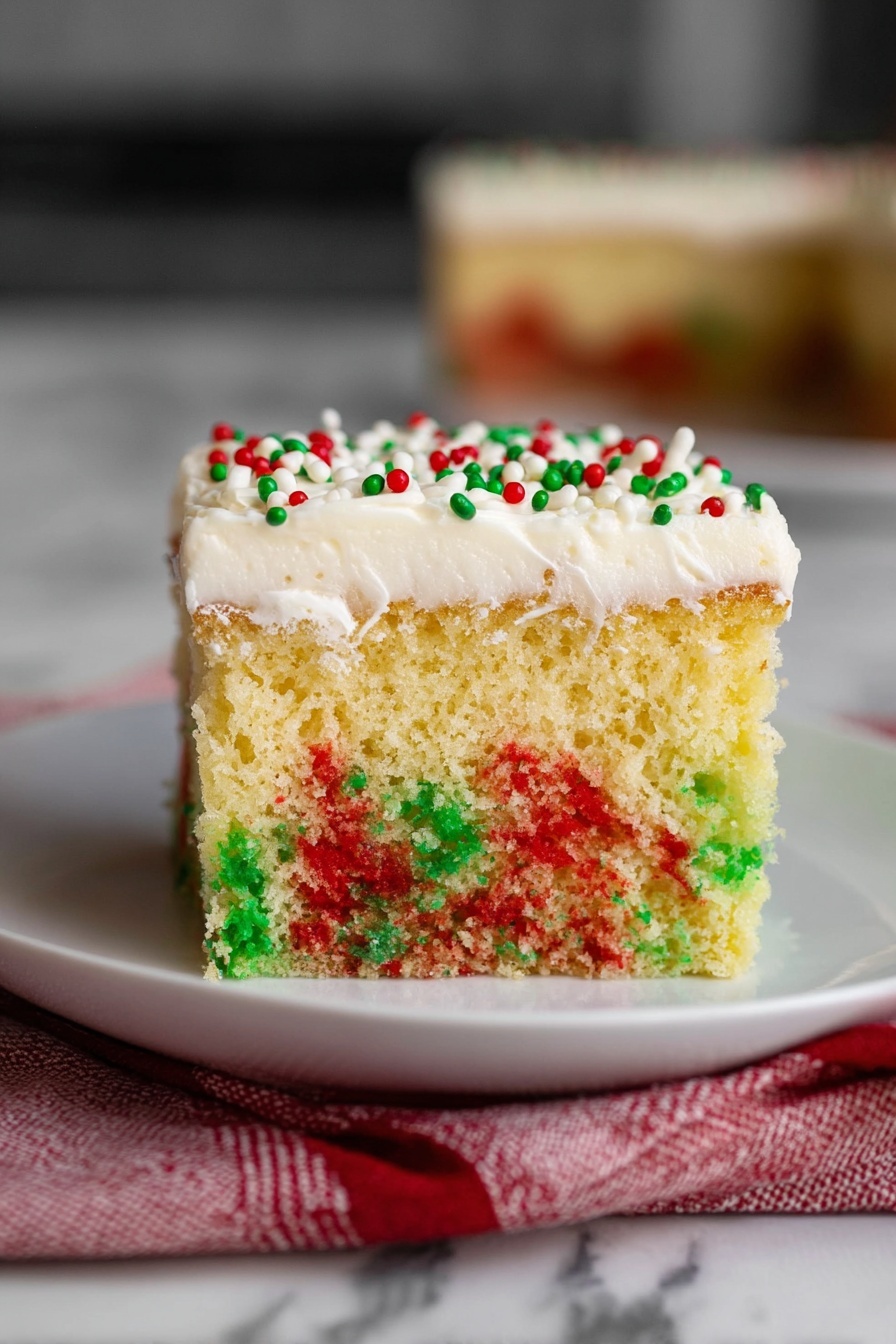 The image shows a square piece of sponge cake with three visible layers. The bottom layer is a light yellow sponge with green and red spots soaked into it, giving a colorful look with a soft, porous texture. The top layer is a thick, creamy white frosting that covers the entire cake surface smoothly. There are small red and green round sprinkles on the frosting. The cake sits on a plain white plate, placed on a white marbled surface with a red and white cloth partially visible underneath. Photo taken with an iphone --ar 2:3 --v 7
