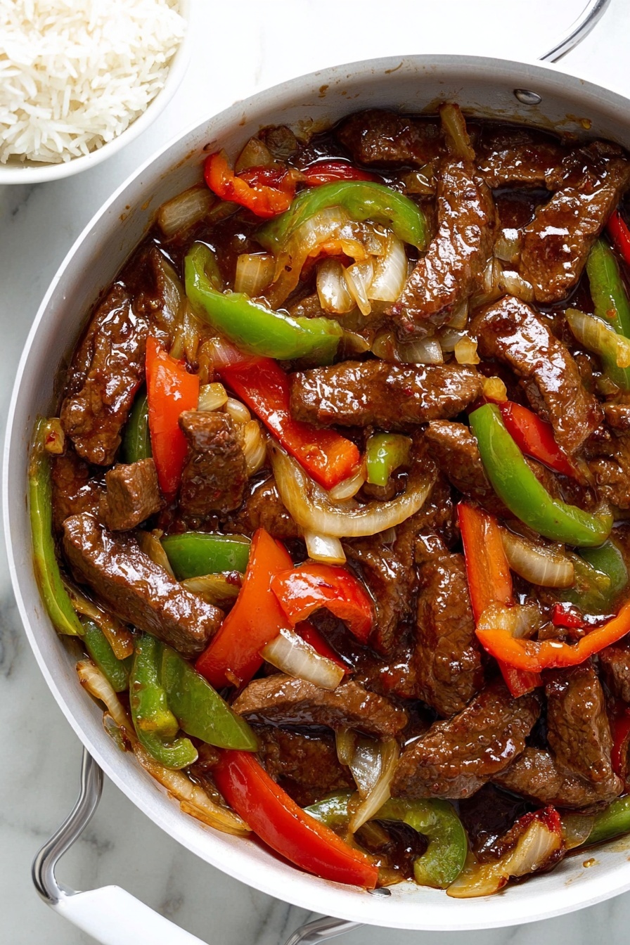The image shows a white pan filled with cooked beef strips coated in a glossy, dark brown sauce, mixed with sliced red and green bell peppers and translucent, soft-cooked onion slices. The beef pieces are irregular in shape and layered throughout the pan, with the colorful bell peppers adding bright red and green tones among the brown meats and sauce. The onions appear tender and slightly caramelized, adding light yellow and off-white shades. The pan is placed on a white marbled surface, with a bowl of white rice partially visible beside it. The overall dish looks rich and saucy with a mix of vibrant vegetables. photo taken with an iphone --ar 2:3 --v 7