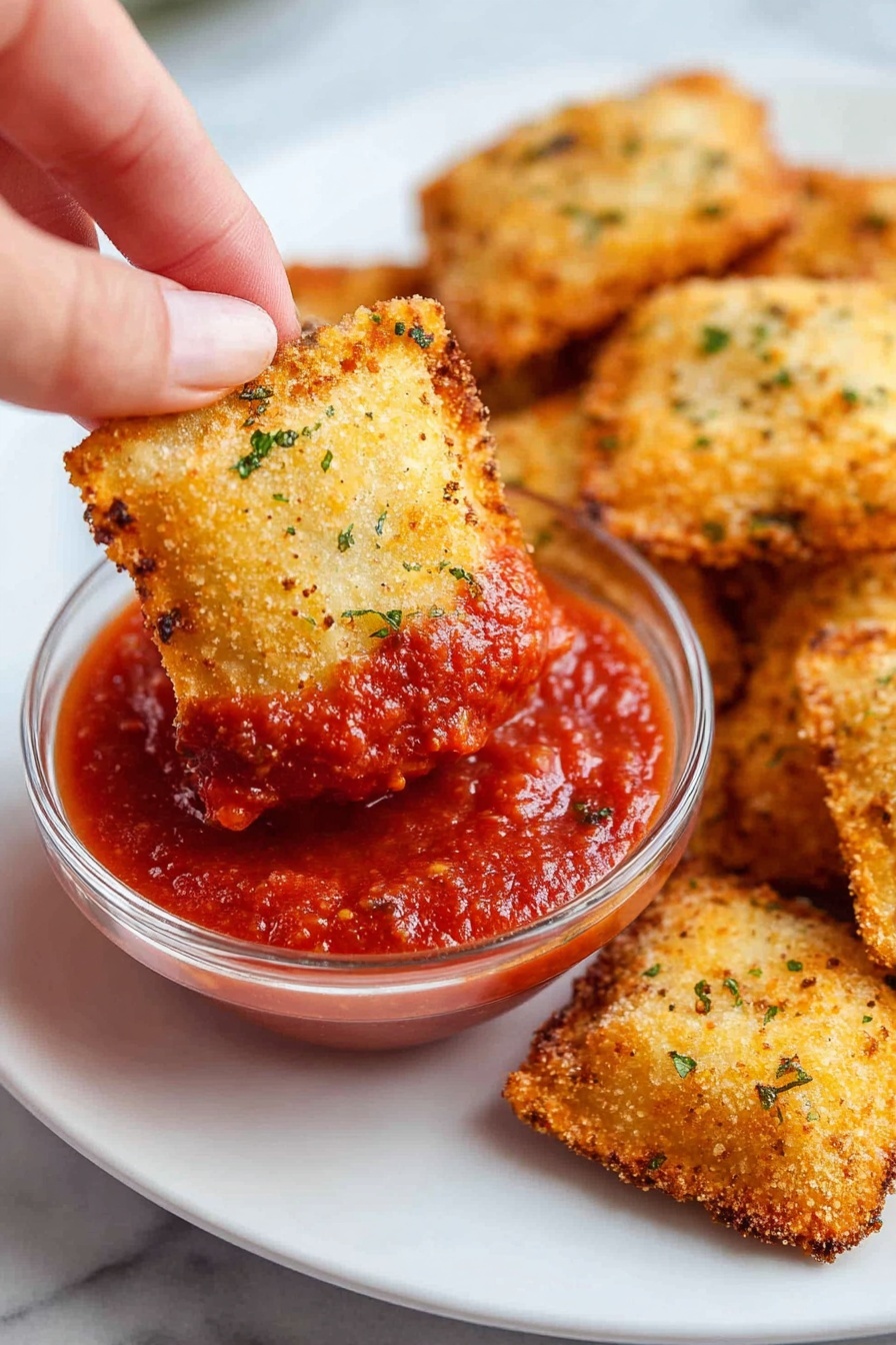 The image shows a close-up of six round ravioli placed on white parchment paper, all arranged neatly on a baking sheet with a dark metal edge. Each ravioli has two visible layers: the bottom pasta layer is a soft yellow color with a smooth texture, and the top layer is covered in a light brown crumb coating with some darker specks scattered throughout. The edges of each ravioli are crimped in a wavy pattern, and there is a slight dome shape in the middle of each piece. Some loose crumbs are sprinkled around the ravioli on the parchment paper. The surface beneath the baking sheet is a white marbled texture. Photo taken with an iphone --ar 2:3 --v 7