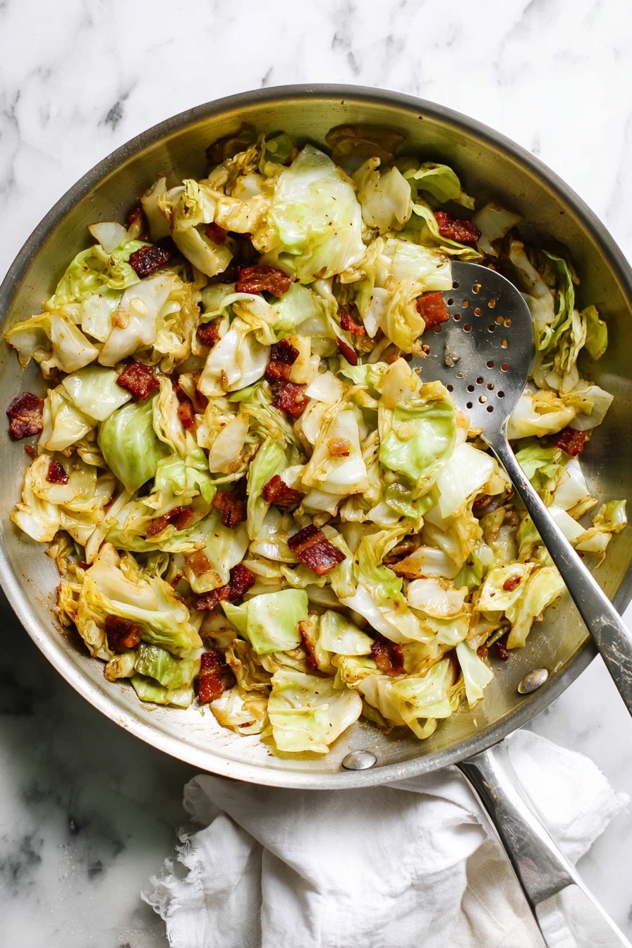 A large silver frying pan filled with cooked cabbage pieces layered unevenly in pale green and light yellow colors, mixed with browned small chunks of bacon scattered throughout. The cabbage looks soft with some edges lightly browned, and bits of onion are visible, adding a golden color. A silver slotted spoon rests inside the pan, shiny and sticking slightly into the cabbage mix. The pan is placed on a white marbled surface with a white cloth nearby. photo taken with an iphone --ar 2:3 --v 7