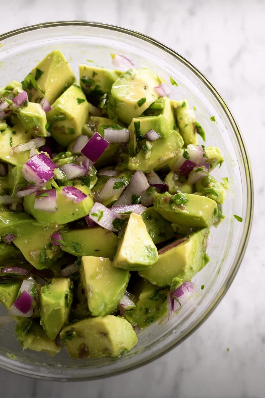 The dish shows two pieces of cooked salmon with a slightly charred, orange-red skin on the bottom layer, revealing tender, flaky, light orange flesh underneath. On top of the salmon is a chunky mix of diced avocado and finely chopped red onions, adding light green and purple colors with a creamy and fresh texture. The food is placed on a white plate with a subtle, smooth surface, and the background features a white marbled texture. photo taken with an iphone --ar 2:3 --v 7