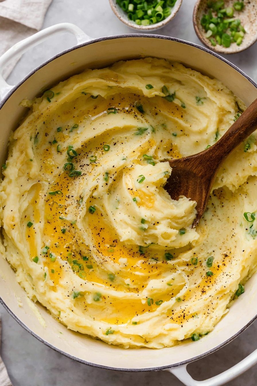 A white pot filled with creamy mashed potatoes mixed with small green onion pieces, swirled smoothly with visible soft folds and a shiny top layer of melted butter that shines golden. Black pepper specks are scattered unevenly over the surface, while a wooden spoon scoops up a portion from the center, showing the thick, fluffy texture. The pot sits on a white marbled surface with some small bowls of green onions and melted butter blurred in the background. Photo taken with an iphone --ar 2:3 --v 7