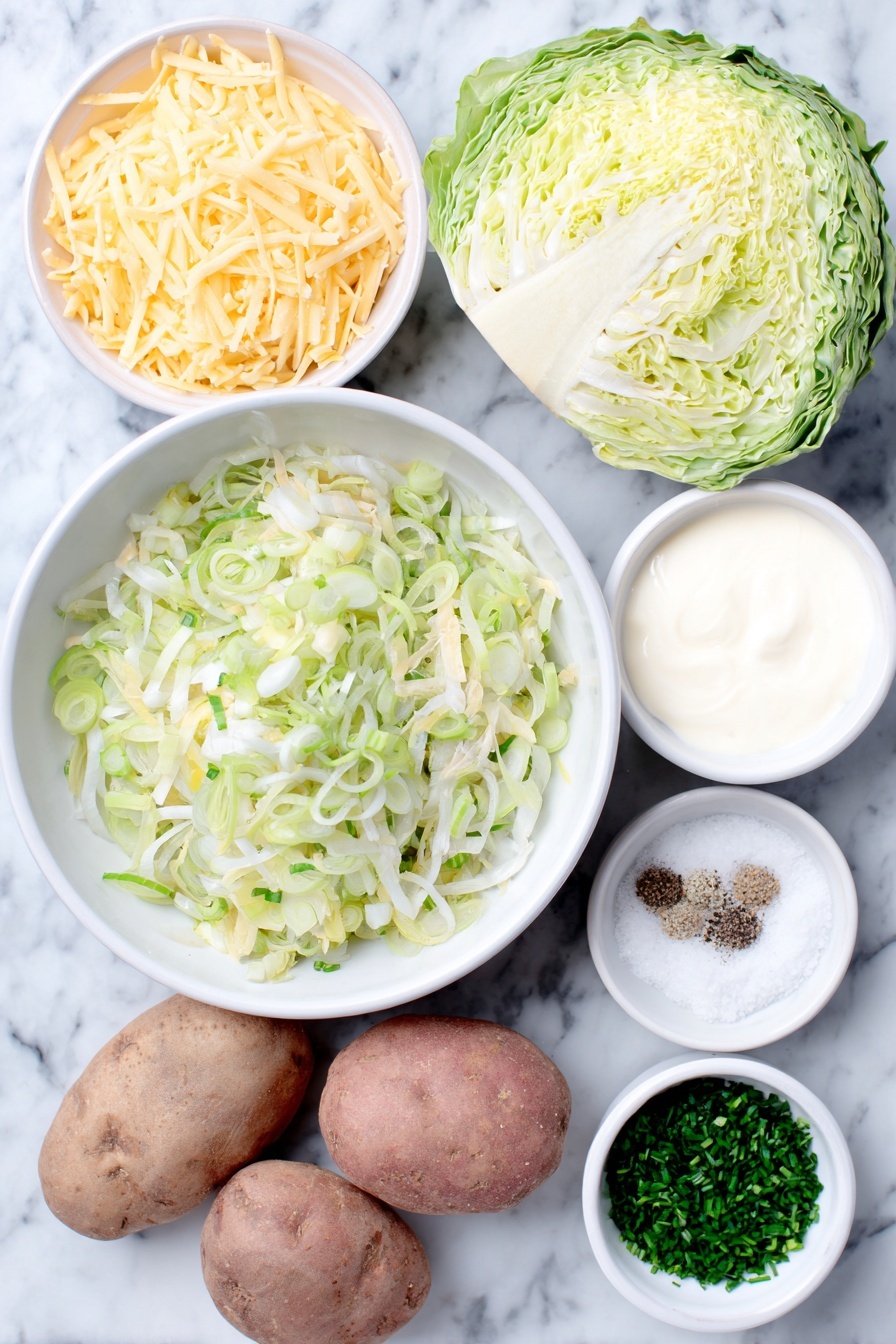 Flat lay of thinly sliced leeks in a simple white ceramic bowl, a small white bowl with minced garlic cloves, a fresh head of green cabbage with some loose leaves, whole uncracked brown russet potatoes, a small white bowl filled with heavy cream, a small white bowl heaped with shredded pale yellow Irish cheddar cheese, a small bunch of bright green parsley sprigs, a small pile of finely chopped chives, a small white bowl with coarse flaky sea salt, a small white bowl holding freshly cracked black pepper placed on a clean white marble surface, soft natural light, photo taken with an iPhone, professional food photography style, fresh ingredients, white ceramic bowls, no bottles, no duplicates, no utensils, no packaging --ar 2:3 --v 7 --p m7354615311229779997